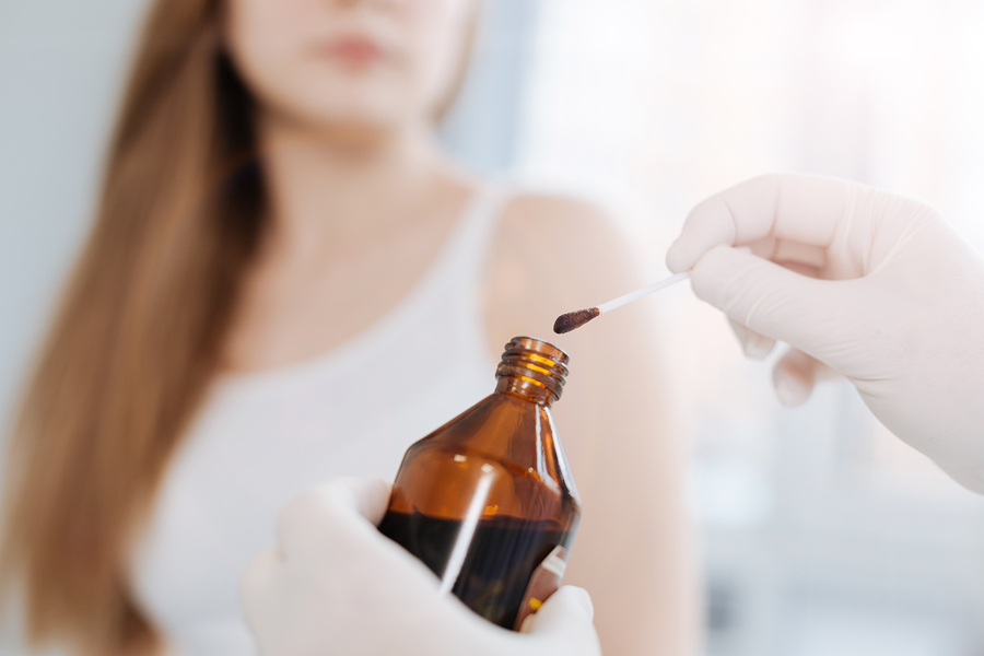 Using iodine for treatment. Concentrated motionless little patient sitting in the hospital and waiting for treatment while dermatologist holding the bottle of iodine